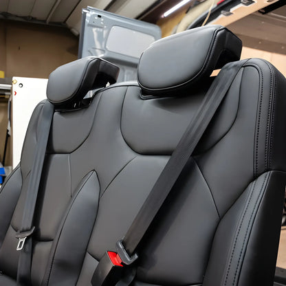Close-up of the NovaLux Duo RS double seat headrests, contoured black backrests and integrated shoulder belts in a workshop.