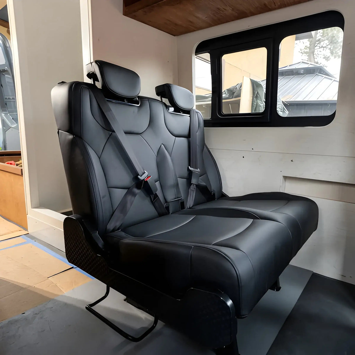 NovaLux Duo RS black double van seat installed beside a camper van window, with two headrests and integrated seat belts.