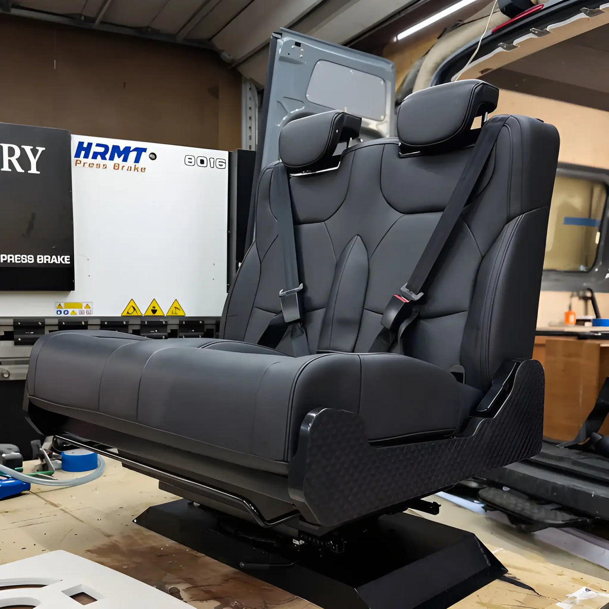 NovaLux Duo RS double swivel seat on a workshop bench, showing the upright backrests, cushions and mounting base.