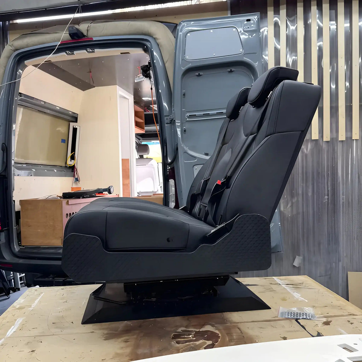 Side profile of the NovaLux Duo RS double seat on a workshop bench, showing the backrest, patterned side panel and swivel base.