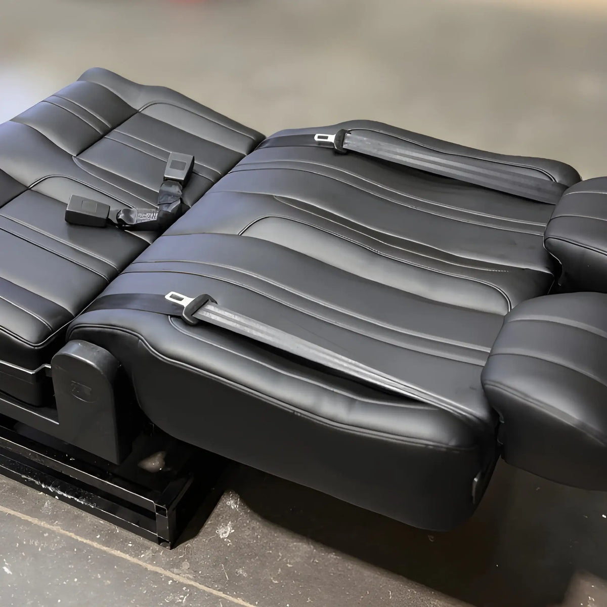 NovaLux Classic double swivel van seat reclined flat for bed conversion, showing black cushions and integrated seat belts.