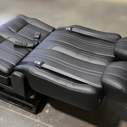 NovaLux Classic double swivel van seat reclined flat for bed conversion, showing black cushions and integrated seat belts.