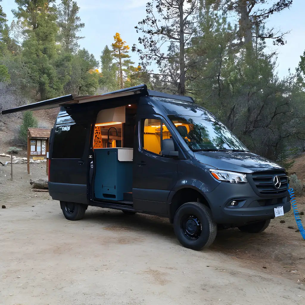 Vantrix side-mounted electric awning extended above the open sliding door of a Mercedes-Benz Sprinter camper van at a wooded campsite.